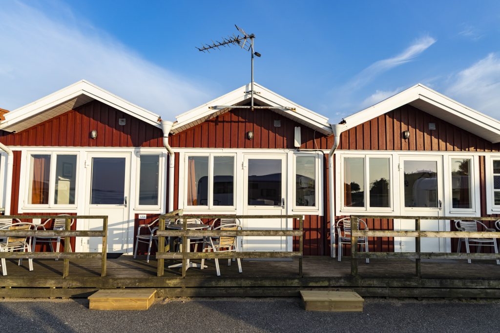 Tre röda stugor med en blå himmel i bakgrunden.