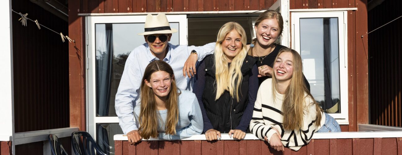 Elever framför röd sjöbodstuga som du/ni kan bo i vid en skolresa/klassresa på Västkusten.