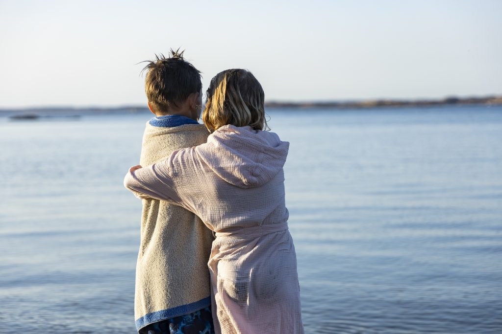 Två barn som ger varandra en kram på stranden på Ramsvik Stugby & Camping, en barnvänlig familjecamping med många familjeaktiviteter, nära Smögen på västkusten.