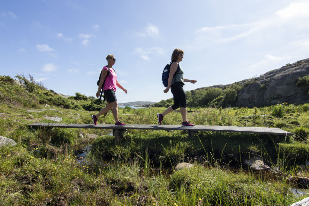 Två tjejer vandrar över en träspång i Ramsvikslandets naturreservat - boka vandringspaket och upplev vandring på Ramsvik.