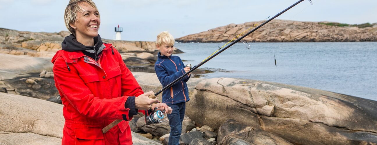 En kvinna i en röd jacka som fiskar med ett barn i bakgrunden.