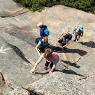 En familj som köpt Ramsvik vandringspaket, som tar sig upp för en klippa.