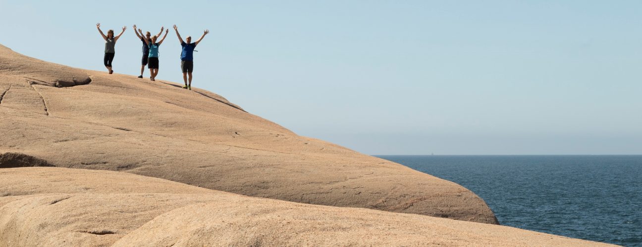 Tre glada personer på en klippa bredvid havet. Kanske är de glada för alla priser och omnämnanden som Ramsvik har fått?