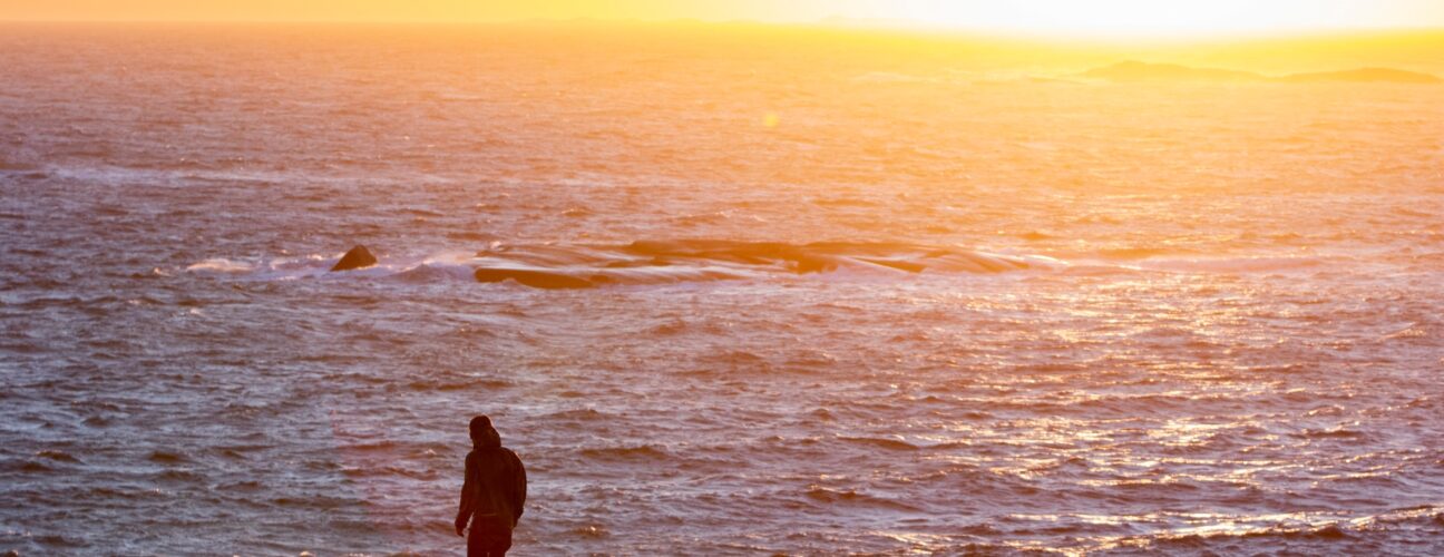 Solnedgång över havet med en person som vandrar.