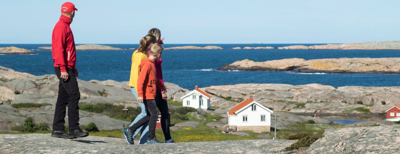 Familj som vandrar med barn med två vita stugor och havet i bakgrunden.