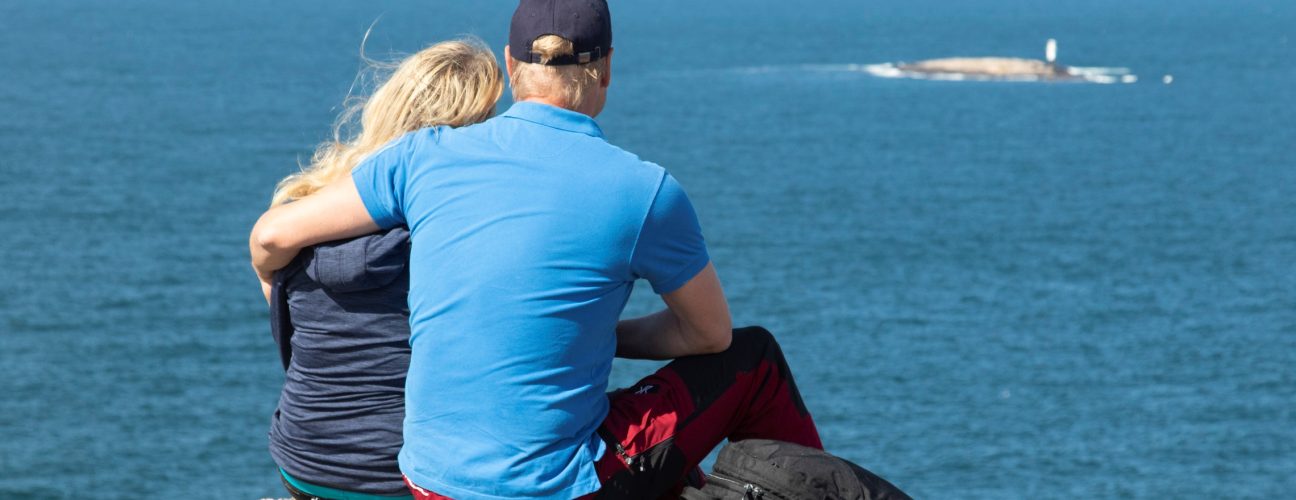 Man och kvinna som sitter på en klippa och ser ut över havet.