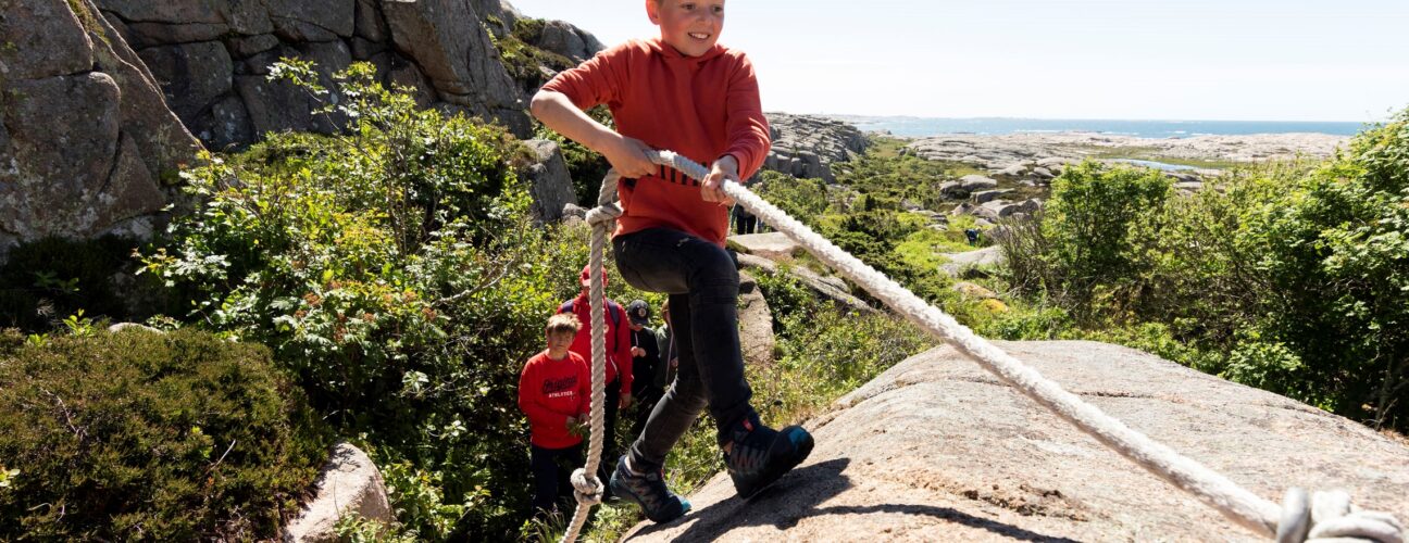 En pojke som klättrar upp för en klippa med hjälp av ett rep.