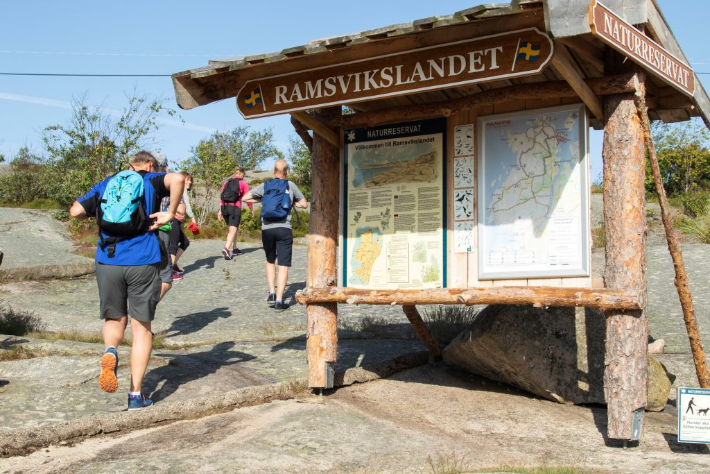 Ett gäng vandrare som går förbi en stor informations-skylt på Ramsvik i Bohuslän på västkusten.