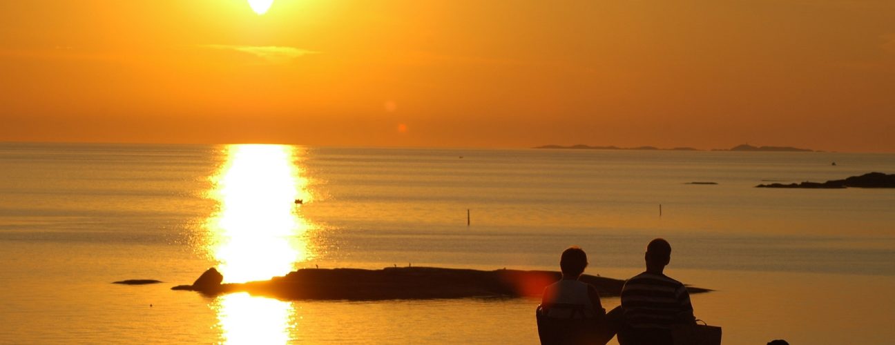 Solnedgång över havet med en familj som sitter och tittar ut på vattnet.
