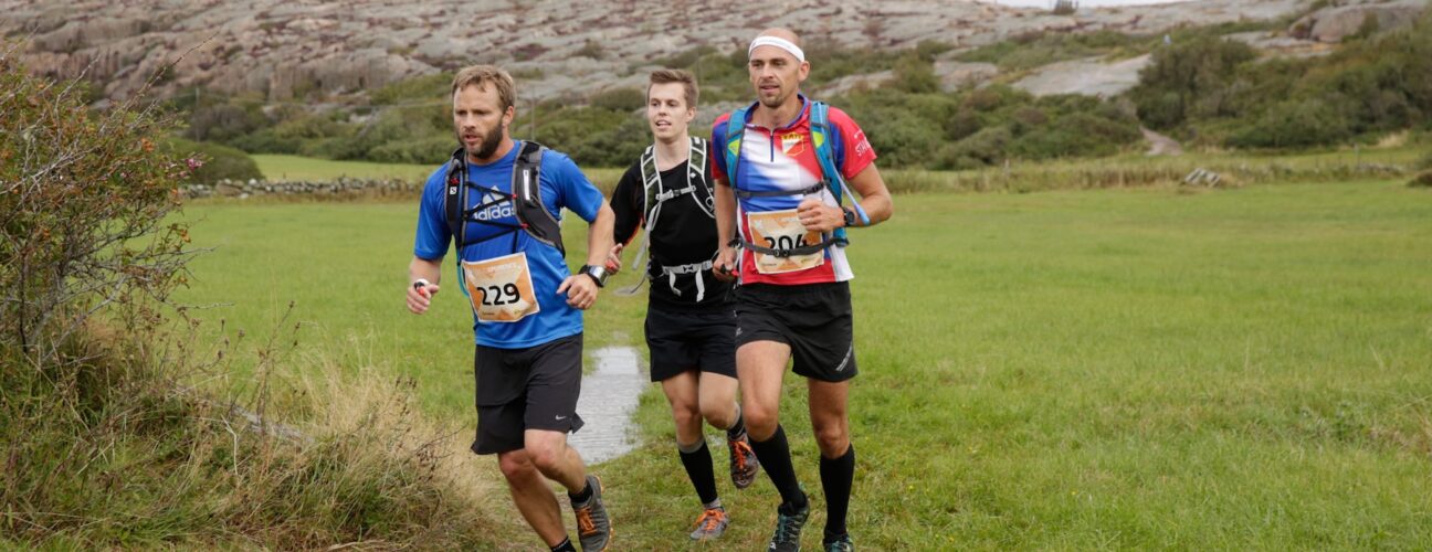 Tre personer som springer på en äng.